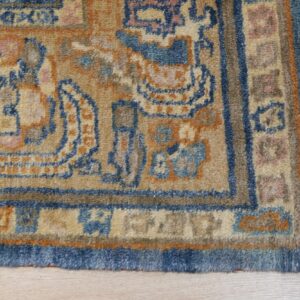 Traditional blue and tan patterned rug with medium pile and fringe rests on light wood planks.