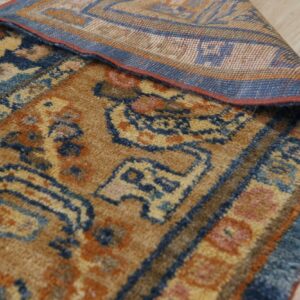 Detail of a gold, blue, and orange patterned rug corner folded back on light wood flooring.