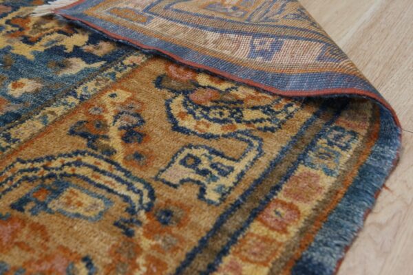 Detail of a gold, blue, and orange patterned rug corner folded back on light wood flooring.