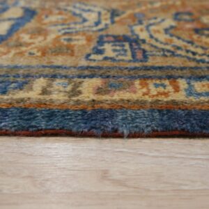 Detail of a low-pile traditional rug with blue and terracotta borders over light blonde wood planks.