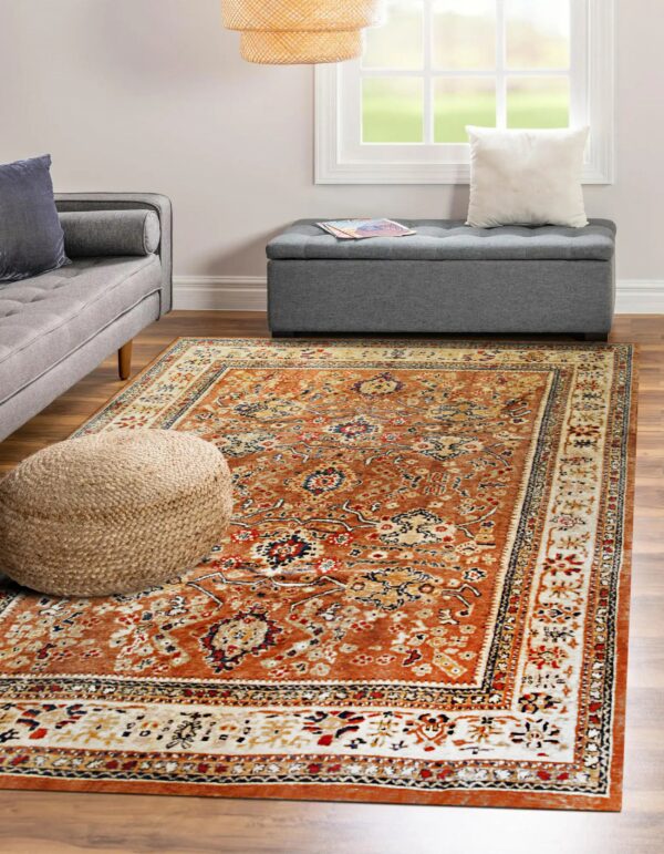 Traditional rust rug with cream, navy, and red accents anchors a room next to a grey tufted ottoman.