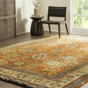 Gold and blue distressed traditional rug with fringe covers wood floor near a dark chair and window.