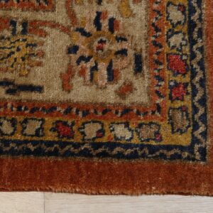 Traditional thick-pile rug corner featuring tan field, rust border, and blue and gold accents on wood.