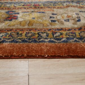 Textured patterned rug in beige, blue, and orange colors with a thick border resting on light wood flooring.