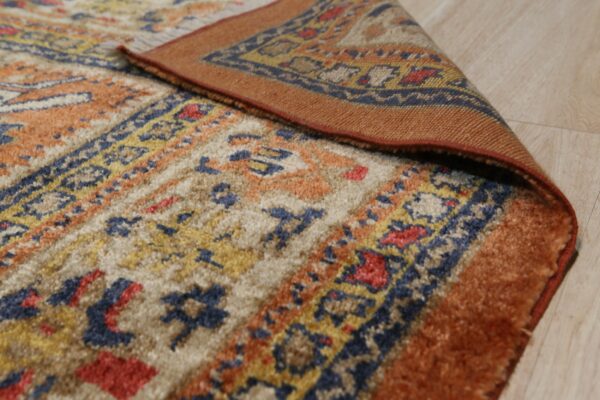 A textured rug in rust, navy, and cream tribal patterns is curled back on light flooring.
