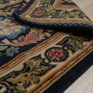 Navy traditional rug with multicolored floral designs rests on a light wood floor, corner curled.