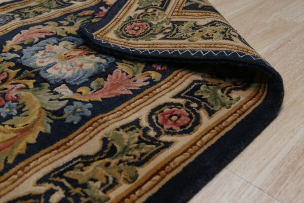 Navy traditional rug with multicolored floral designs rests on a light wood floor, corner curled.