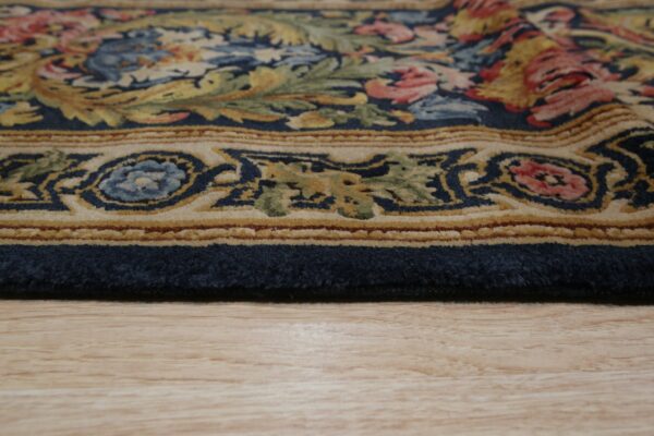 The plush edge of a navy, beige, and multicolor floral rug rests on light wood planks.