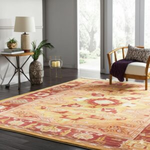 Traditional floral rug in tones of gold and rust red on dark floors in a brightly lit living area.