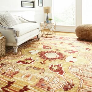 Ocher and deep red ornate rug anchors a bright living room featuring a white upholstered armchair and wood floor.