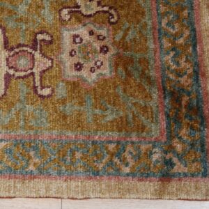 Textured golden rug detail with traditional patterns, burgundy accents, teal border, and light fringe.