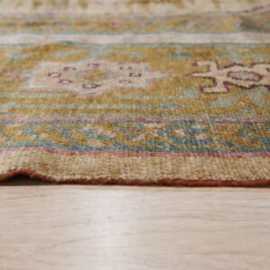 A close-up shows a patterned rug in gold, teal, and maroon resting on a light beige wood floor.