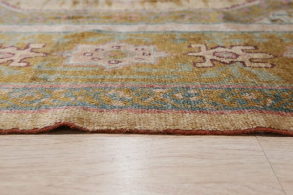 A close-up shows a patterned rug in gold, teal, and maroon resting on a light beige wood floor.