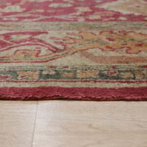 Medium pile rug featuring a detailed red, gold, and beige pattern resting on light wood flooring.