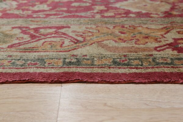 Medium pile rug featuring a detailed red, gold, and beige pattern resting on light wood flooring.