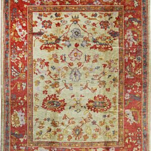 A traditional rug featuring a pale olive field and a wide patterned border of rust red.