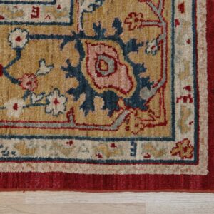 Traditional rug detail showing golden field, red border, and blue floral pattern on light wood floor.