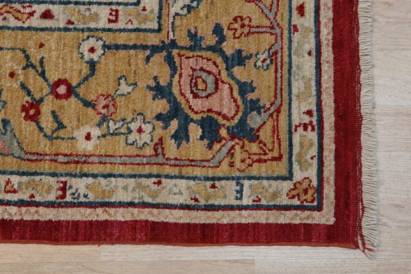Traditional rug detail showing golden field, red border, and blue floral pattern on light wood floor.