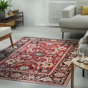 A traditional red and dark brown floral rug centers a modern living room with beige seating and light wood floors.