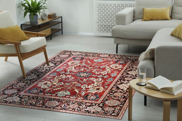 A traditional red and dark brown floral rug centers a modern living room with beige seating and light wood floors.