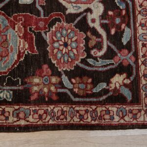 Close-up of a dark brown rug border showing red, blue, and cream floral designs on light wood.