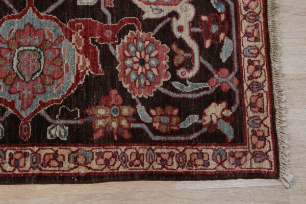 Close-up of a dark brown rug border showing red, blue, and cream floral designs on light wood.