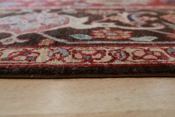 Close-up of a patterned rug in brown, red, blue, and cream on light wood planks.