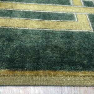 Deep green plush rug with yellow geometric patterns sits on light wood flooring.