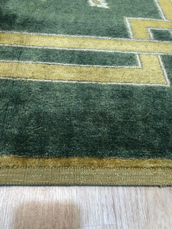 Deep green plush rug with yellow geometric patterns sits on light wood flooring.
