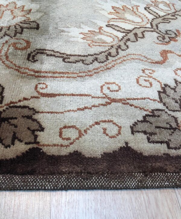 Textured high-pile rug with flowing floral motifs in cream, taupe, and deep brown on light wood flooring.