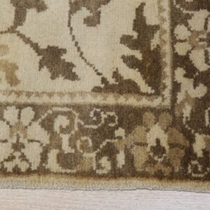 Cream and brown traditional rug border with fringed edge rests on light wood plank flooring.