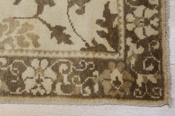 Cream and brown traditional rug border with fringed edge rests on light wood plank flooring.