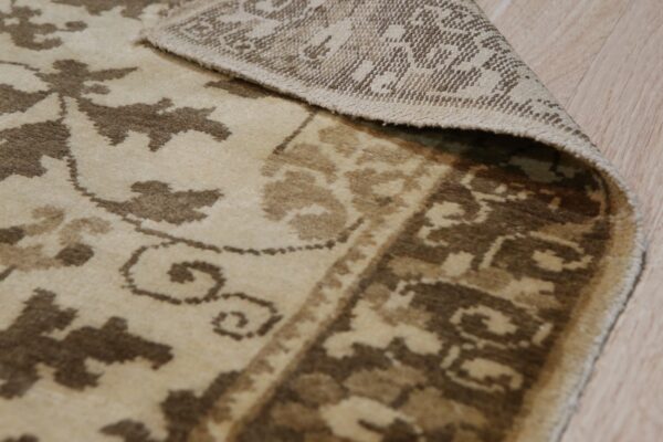 Light brown and beige floral rug curled on wood planks, exposing the woven backing.
