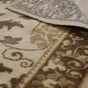 Beige and brown floral patterned rug curled to show the woven backing on light wood flooring.