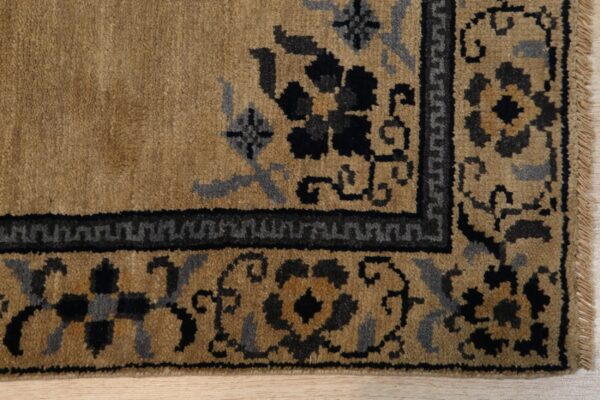 Tan pile rug with black and slate gray floral and geometric border detail on light wood floor.