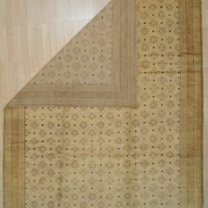 Beige rug featuring a geometric pattern and Greek key border is folded over on light wood planks.