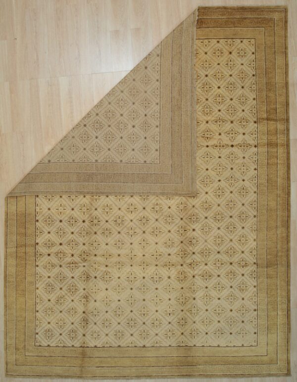 Beige rug featuring a geometric pattern and greek key border is folded over on light wood planks.