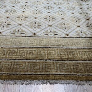 Beige and brown rug displaying diamond motifs and a border with repeated meander patterns on wood.