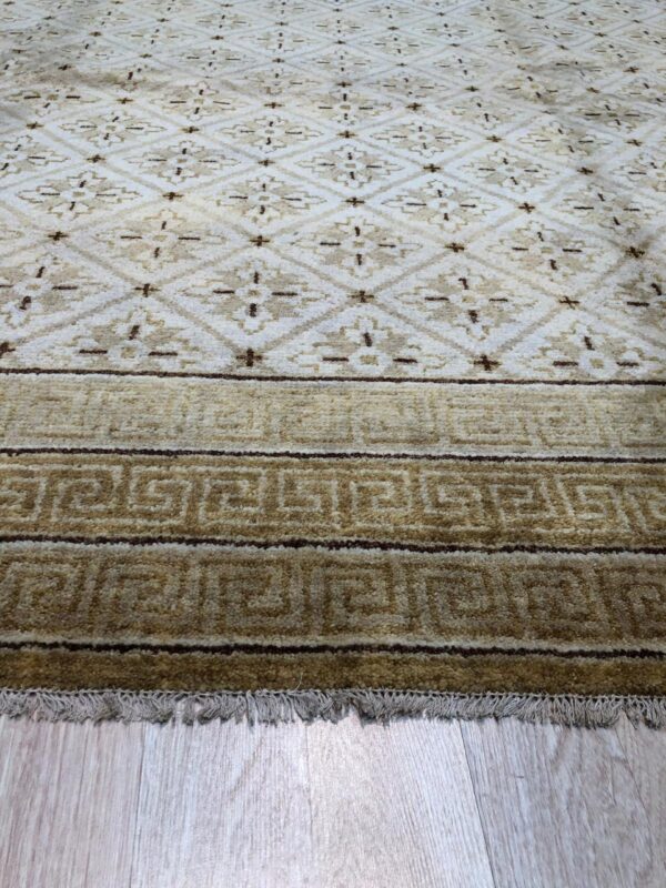 Beige and brown rug displaying diamond motifs and a border with repeated meander patterns on wood.
