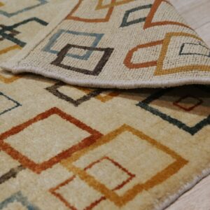 Textured beige rug featuring interlocking geometric lines in rust, gold, brown, and teal on wood floor.