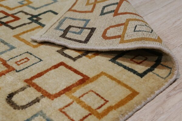 Textured beige rug featuring interlocking geometric lines in rust, gold, brown, and teal on wood floor.