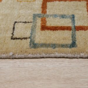 A cream rug with high pile and rust and blue geometric shapes rests on light wooden flooring.