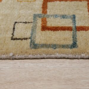 Beige medium pile rug with blue, rust, and brown geometric squares rests on light wood grain floor.