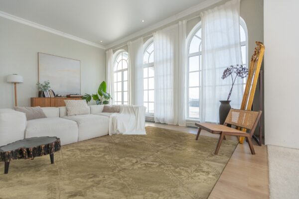 A muted khaki rug with subtle ornate patterns anchors a modern living space with light wood floors.