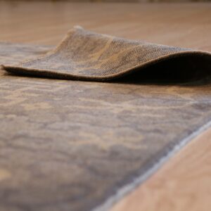 Muted beige and grey patterned rug edge is curled up on a light hardwood floor.