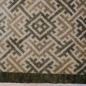 Textured rug with cream and olive geometric diamonds framed by a solid dark green border on wood planks.