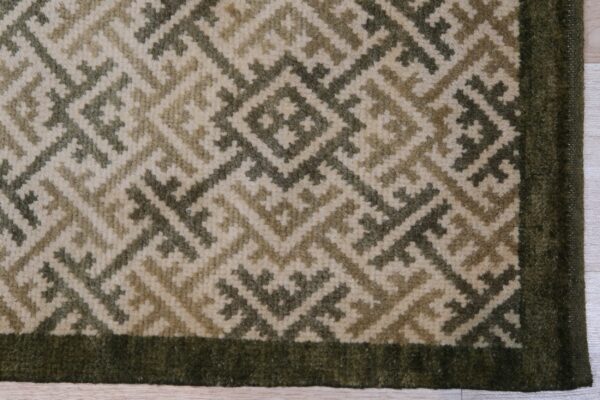 Textured rug with cream and olive geometric diamonds framed by a solid dark green border on wood planks.