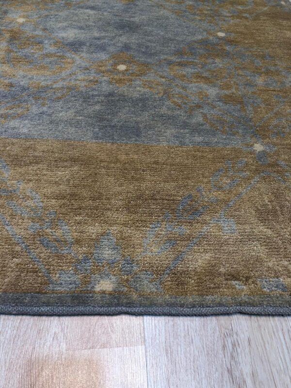 A high-pile rug with blue and brown distressed floral patterns rests on light plank flooring.