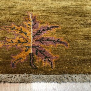 Textured gold rug featuring an orange and magenta leaf pattern and beige fringe on wood flooring.