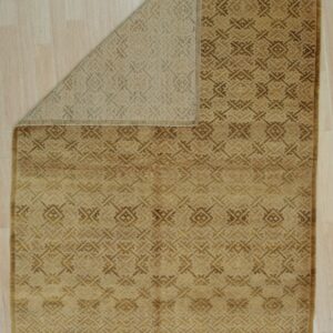 Golden brown rug with a repeating geometric pattern is folded back, revealing the tan backing on light wood flooring.